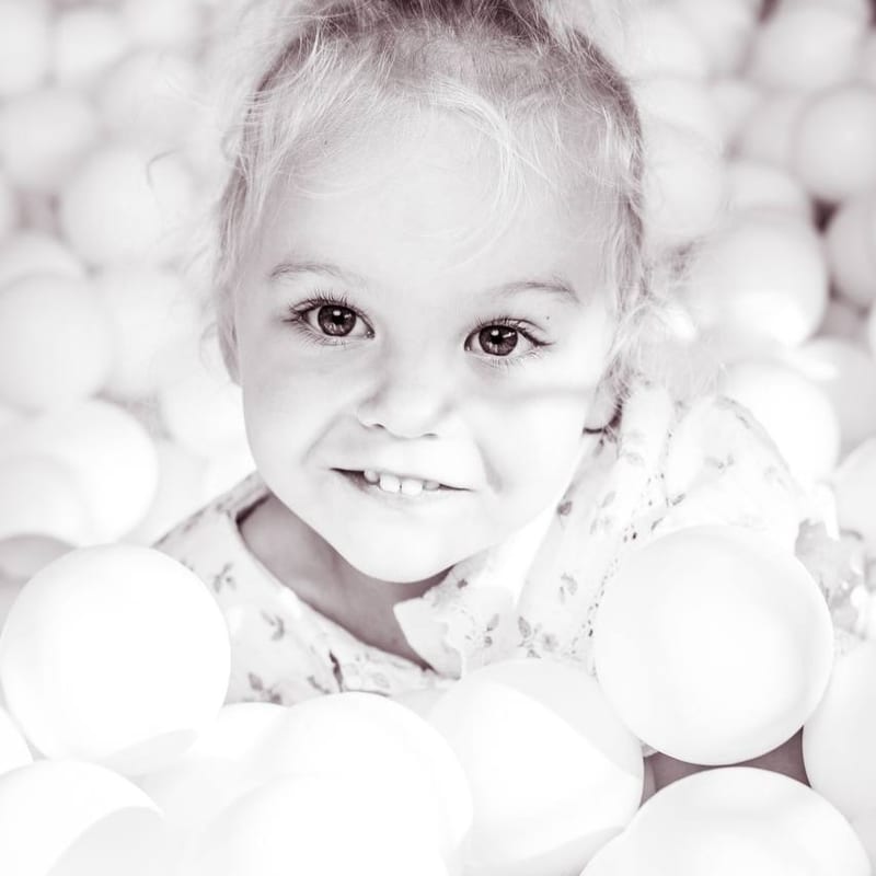 Anya sonriendo entre bolas de un parque infantil, en blanco y negro suave
